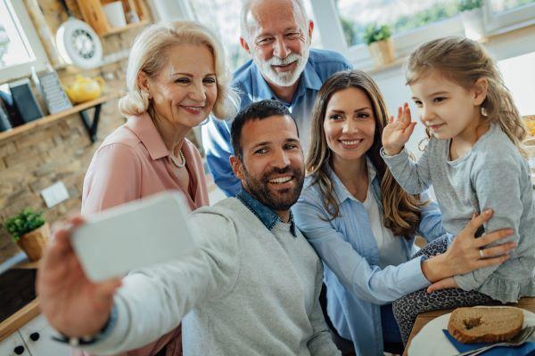 Une famille heureuse, grands-parents à leur petite fille, s’amuse ensemble en prenant un selfie  avec un téléphone portable, dans une cuisine.